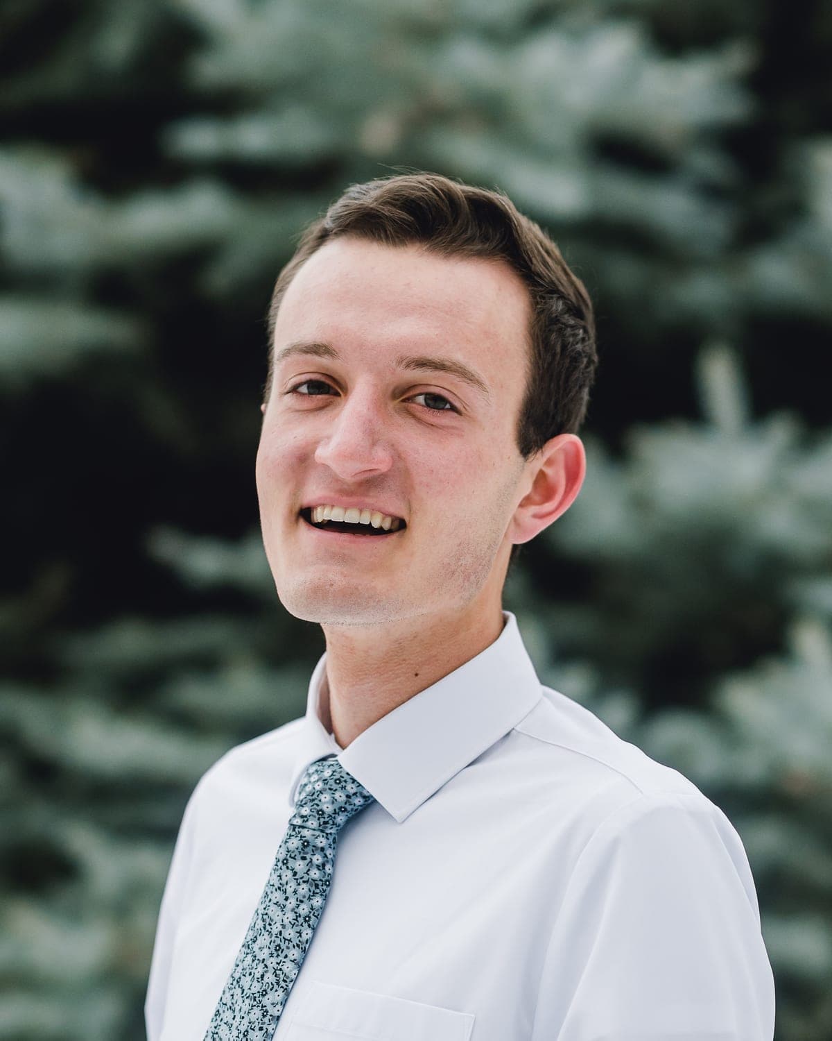 Foster Curtis, freelance web developer, in a white shirt and tie outdoors in front of an evergreen